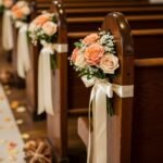 Peach roses and white ribbons decorating the ends of wooden church pews for a wedding.