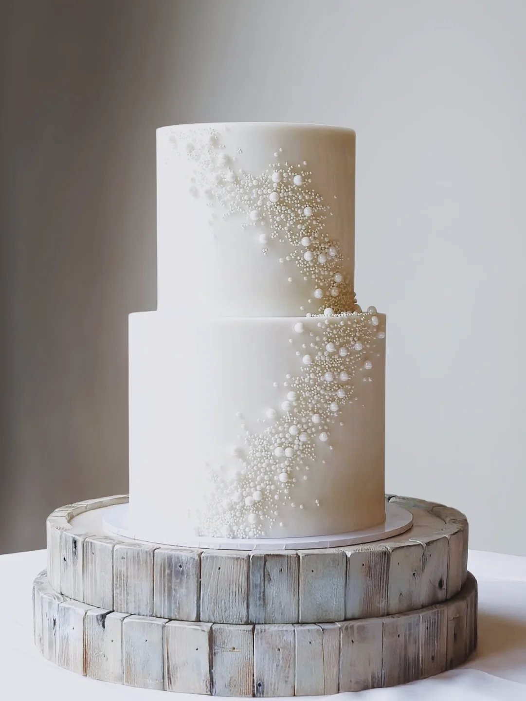 Two-tier white wedding cake decorated with cascading white pearls on a rustic wooden stand.