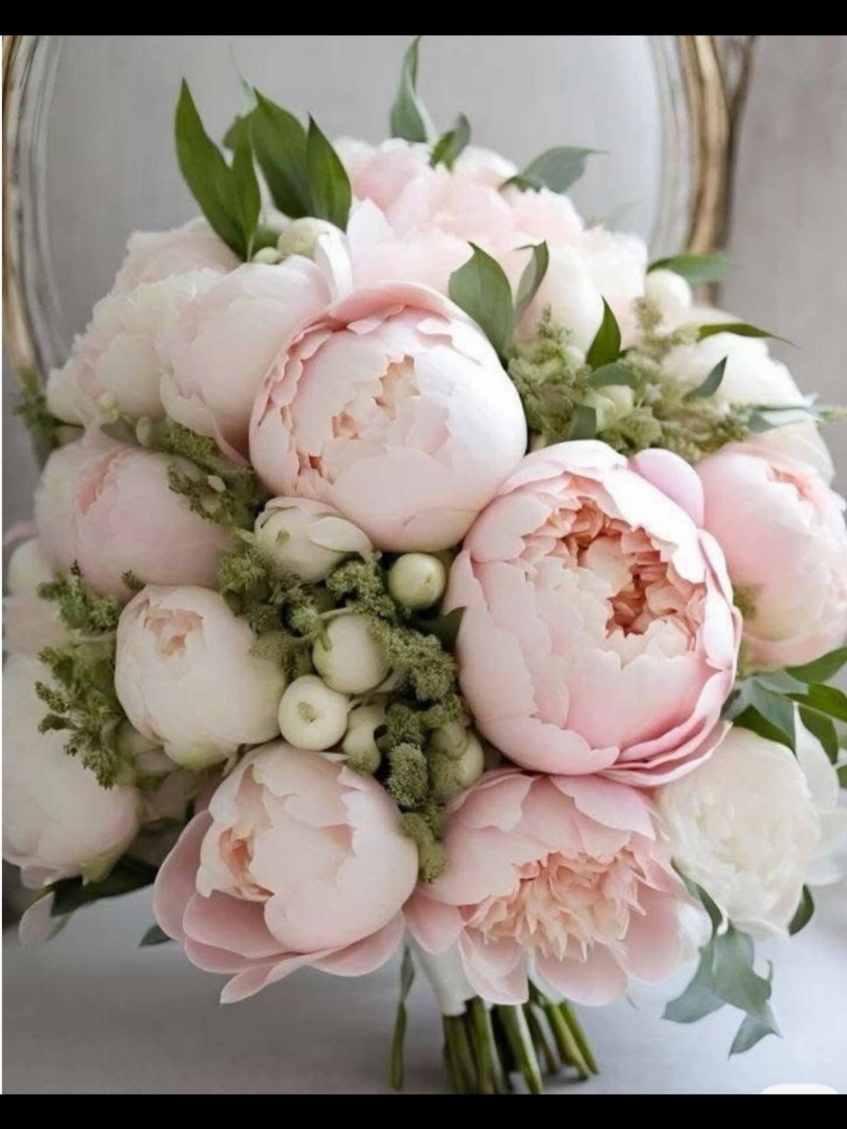 A large bouquet of pale pink and white peonies with green foliage and small white berries.
