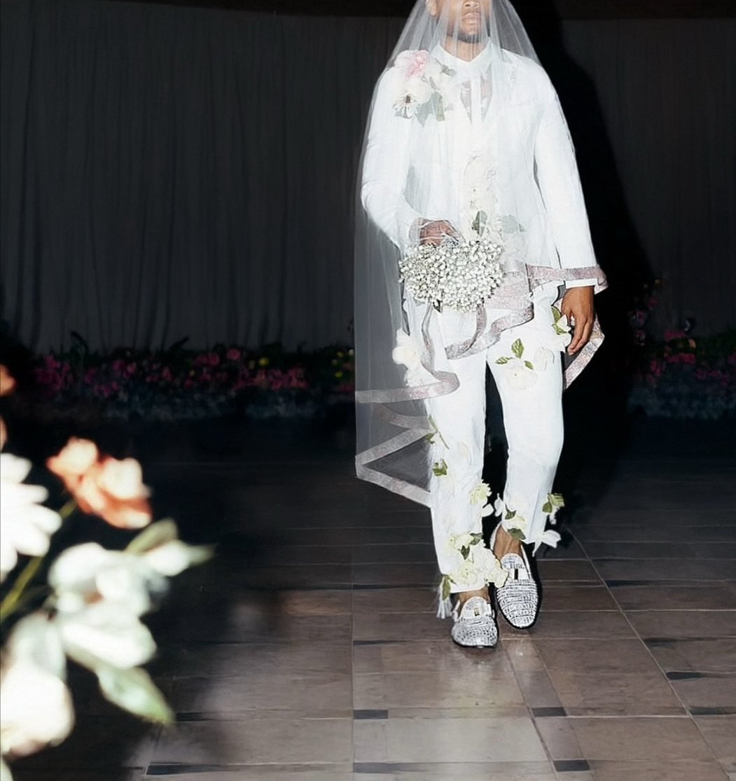 Person in white wedding attire with a veil, floral bouquet, and sparkly silver loafers.