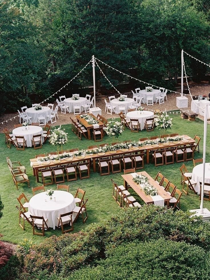 Outdoor wedding reception with round and rectangular tables decorated with white flowers on a green lawn.