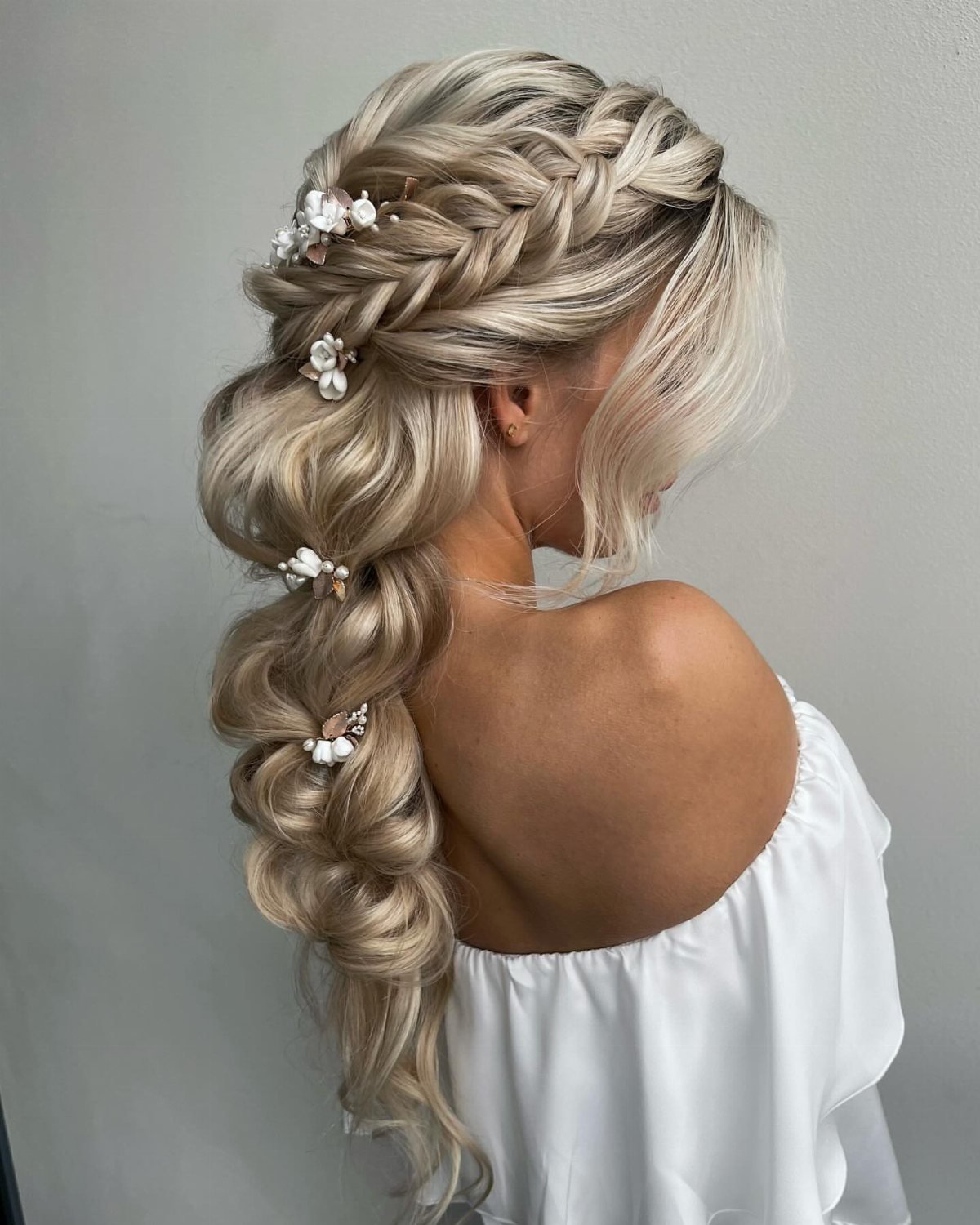 Blonde woman with an intricate braided hairstyle decorated with small white floral hair accessories.