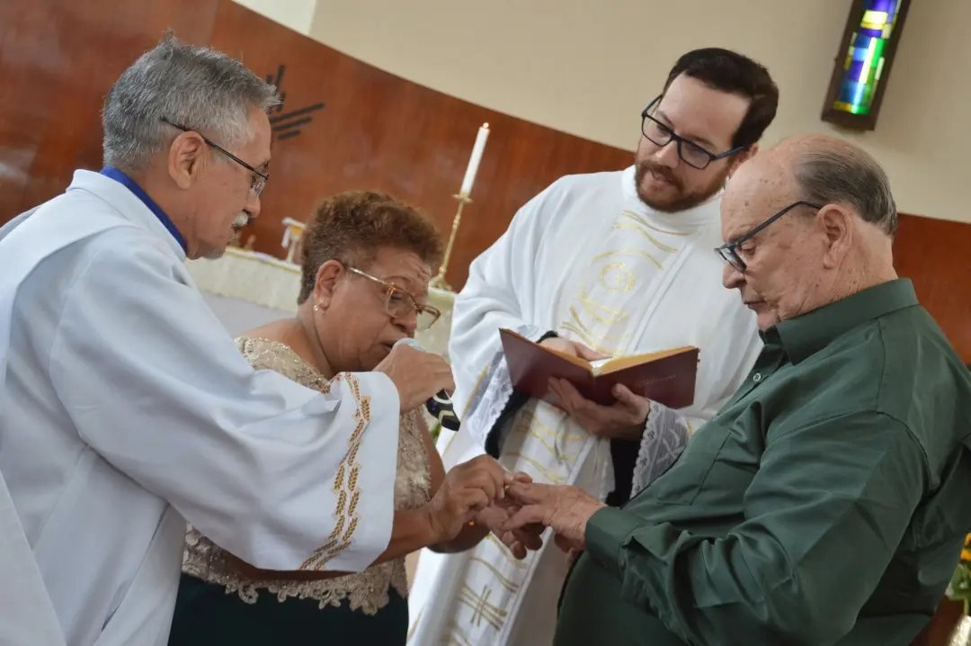 An elderly man receives a ring on his finger during a ceremony in a church.