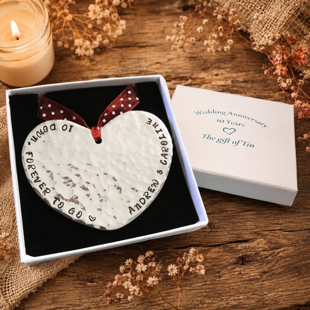 A heart-shaped hand-hammered tin piece with engraved names inside a gift box.