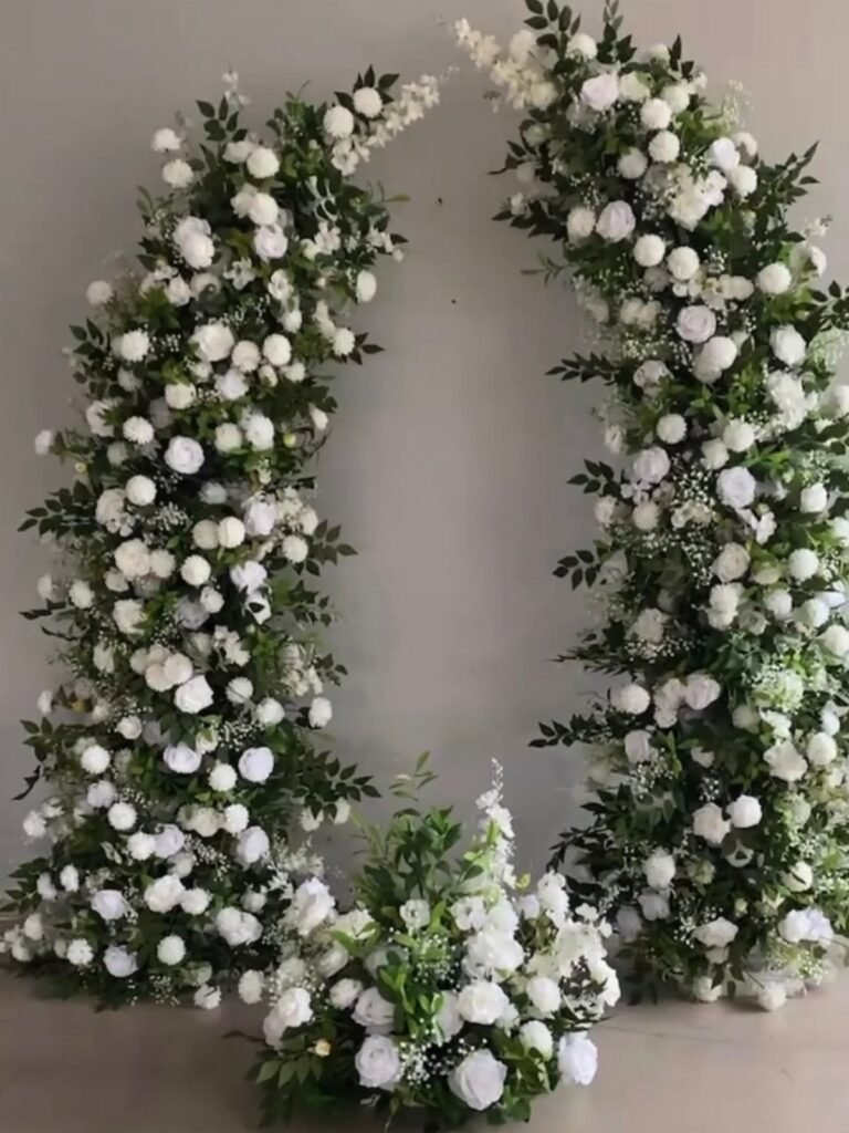 A large circular wreath made of white roses and green foliage against a grey wall.