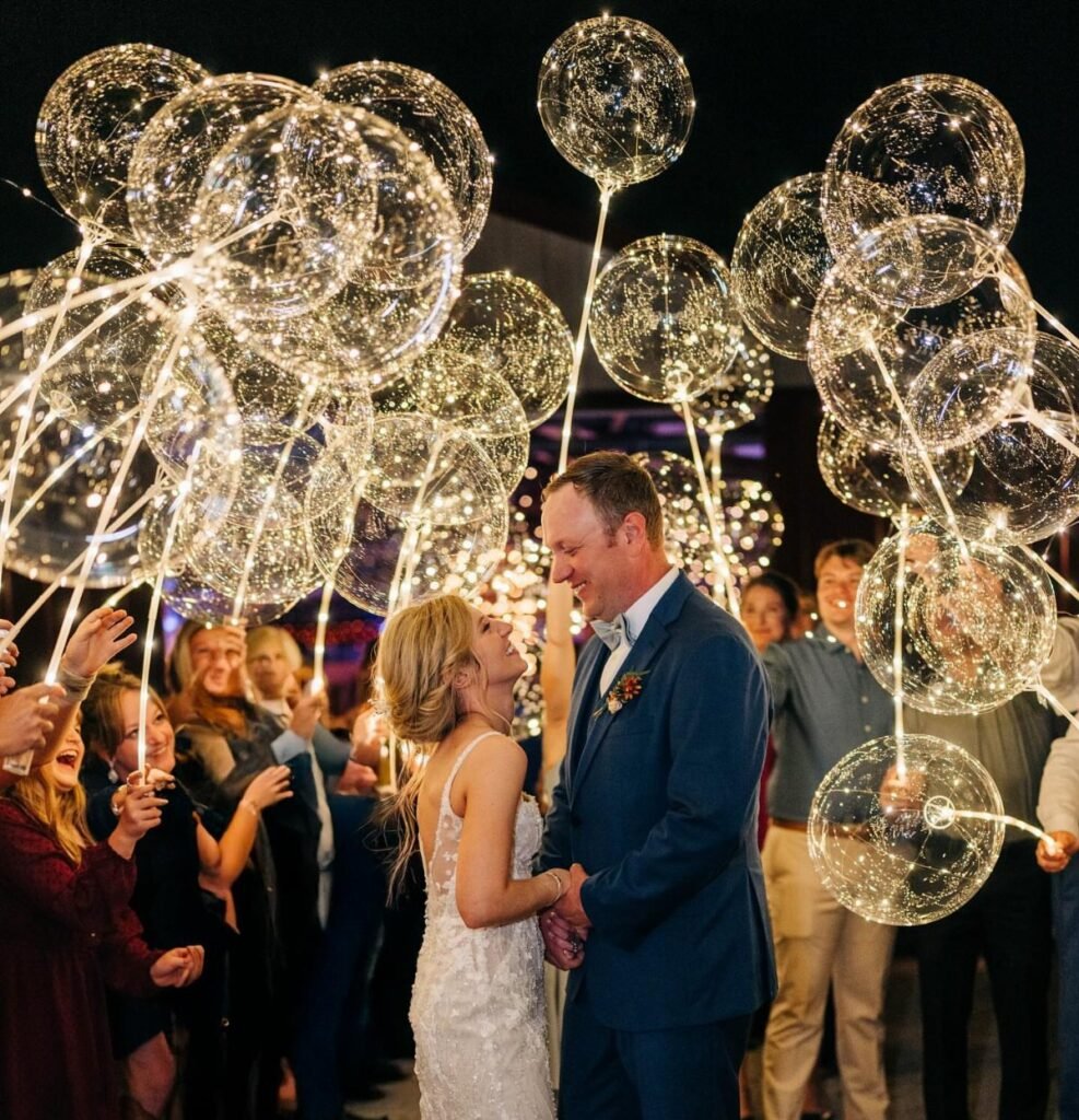 Bride and groom smiling at each other surrounded by guests holding glowing fairy light balloons.